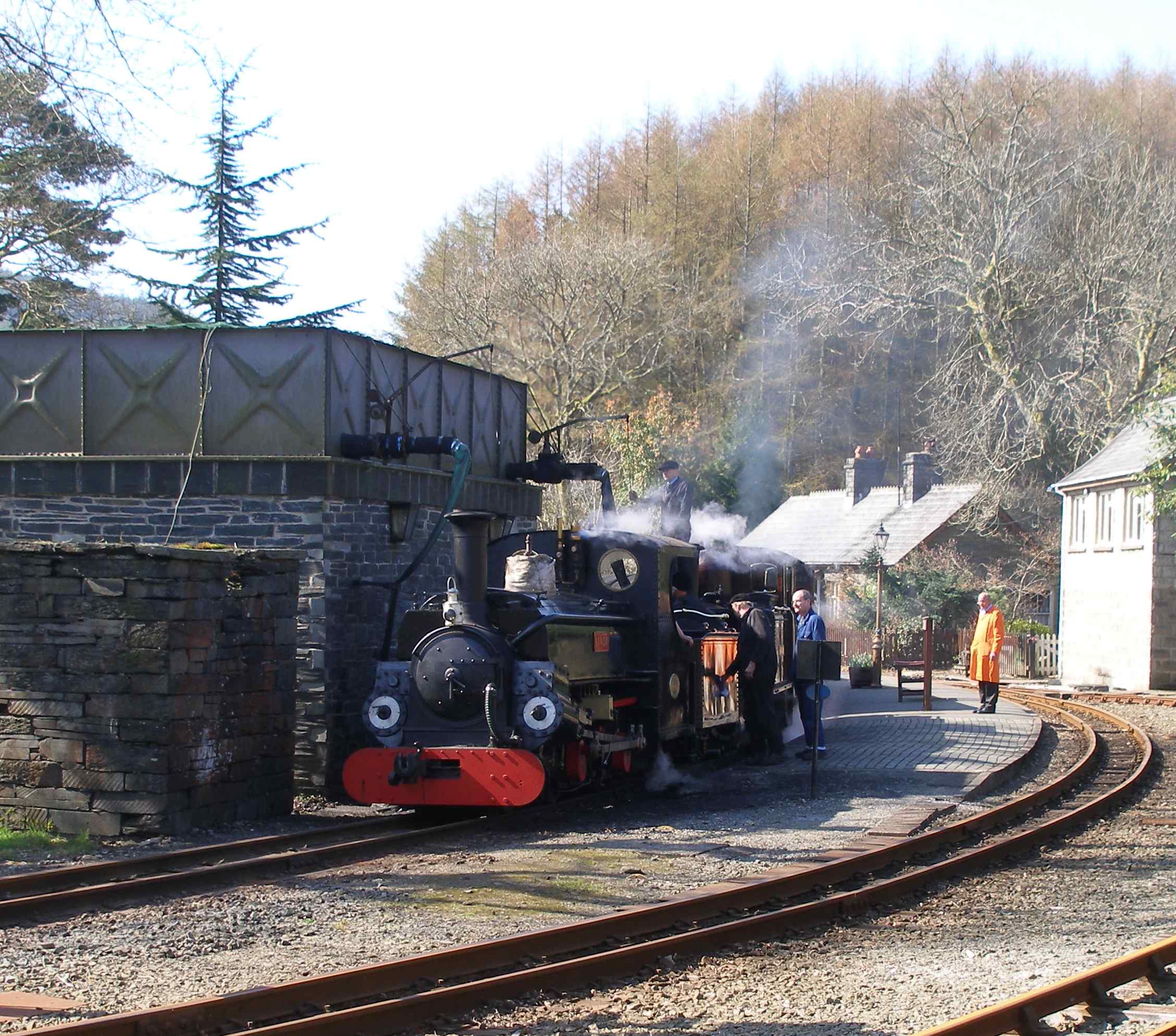 'Merddin Emrys' and 'Linda' stand at the water tank at Tan-y-Bwlch. The driver can be seen in the act of removing the Lancashire & Yorkshire Railway badge from the tender (shame!). This reflected the origins of the restoration team, who hailed from the two counties mentioned. The breeze block structure to the right was constructed as a signal box, very much in the style of one that featured in Meccano's Bayko construction set as it features domestic window frames. There was a set of GWR signal box windows that sat in the car park for some time, but were ultimately not used. The structure now houses the relays to work the automated signalling at this location. 