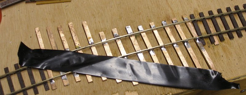 Curved OO diamond crossing build with the first track completed, and the alignment of the second marked with insulation tape.