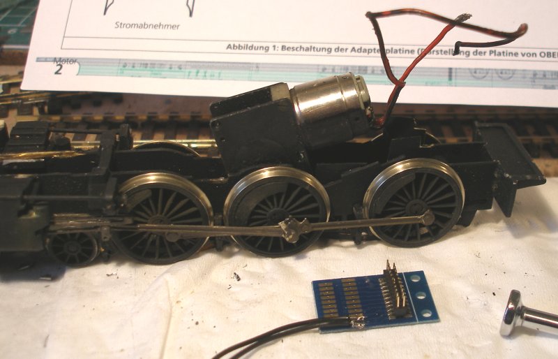 The DJH Caprotti Standard 5 Portsecap-fitted chassis with pick-up wires pulled through and cut, and the new pick-up wires soldered to the adapter. Note the ESU wiring diagram proped up behind.